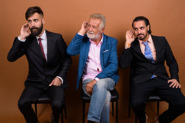 Wall Mural - Three multi ethnic bearded businessmen together against brown background