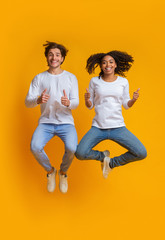 Poster - Joyful interracial couple jumping in the air and gesturing thumbs up