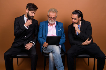 Wall Mural - Three multi ethnic bearded businessmen together against brown background