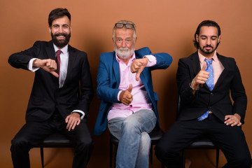 Wall Mural - Three multi ethnic bearded businessmen together against brown background