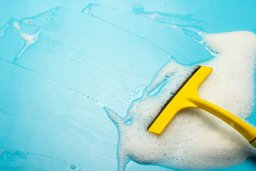 Scraper for cleaning and wipes soap suds on a blue background. Cleaning concept, cleaning service. Banner. Flat lay, top view