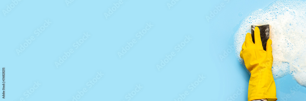Hand in a yellow rubber glove holds a cleaning sponge and wipes a soapy foam on a blue background. Cleaning concept, cleaning service. Banner. Flat lay, top view - obrazy, fototapety, plakaty 