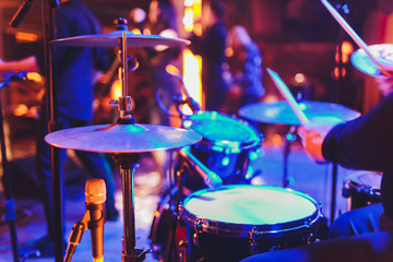 The man is playing drum set in low light background.