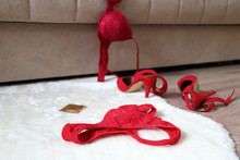 Sex Concept, Red Lace Panties, Bra, Condom And Shoes On High Heels On The Fur Rug On A Floor Near Sofa. Romantic Night Of Passion, Female Lingerie