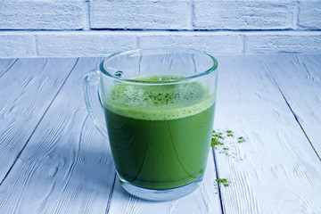 Japanese green tea Matcha in a transparent glass mug close up on a white wooden table against a brick wall