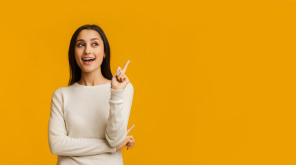 young brunette woman pointing finger up, having idea over yellow background