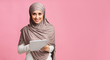 Millennial muslim girl in hijab with digital tablet over pink background