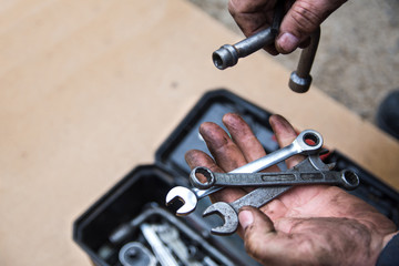 Wall Mural - A male mechanic is sorting out wrenches in a box with tools for repair of faulty equipment. Hands smeared with grease are holding various wrenches. Workshop and repairing