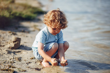 Beautiful little boy in a blue shirt. Childred playing in a summer beach. On a sand