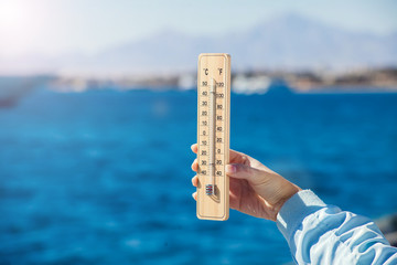 Fototapete - Thermometer in hand in front of sea background. Weather forecast concept