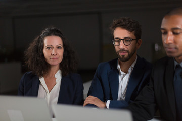 Business colleagues using laptops in dark office. Professional multiethnic business people using laptop computer while working late at night, selective focus. Overworking concept