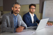 © Mangostar - Two handsome businessmen looking at camera. Cheerful bearded manager sitting at table and holding pen. Business, working late concept