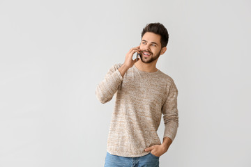 Happy young man talking by mobile phone on grey background