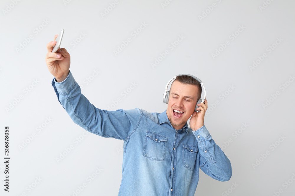 Handsome young man with headphones taking selfie on light background
