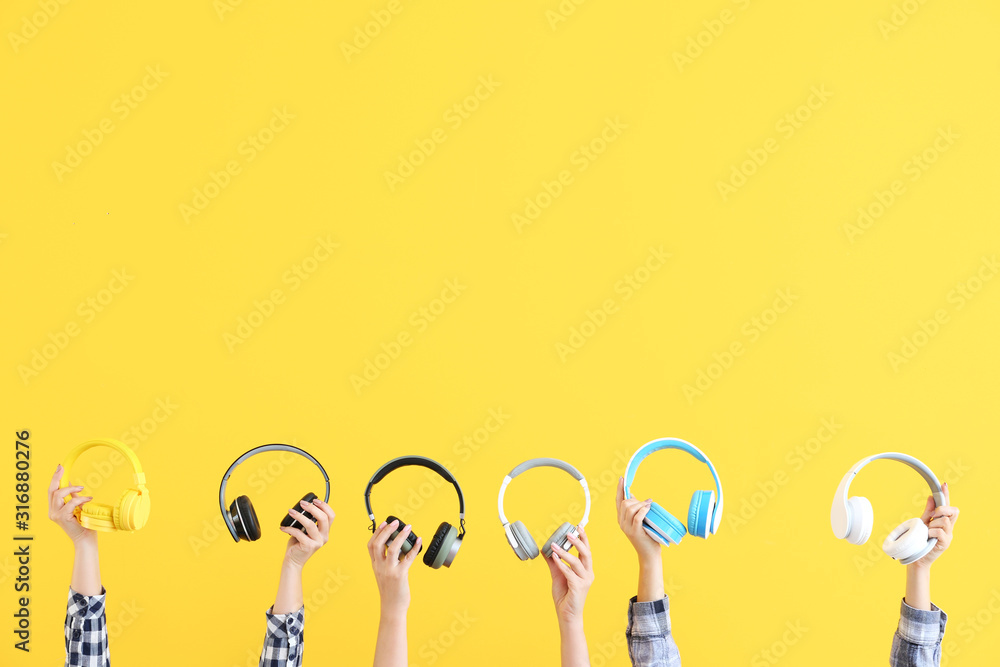 Hands with modern headphones on color background