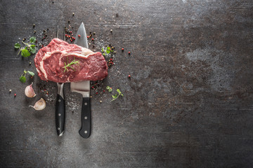 Raw beef steak with fork and knife salt pepper and herbs on dark concrete background