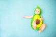 Cute smiling baby in an avocado suit lies on a blue background
