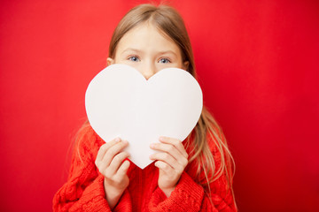 Lovely little girl holding large paper heart, over red background