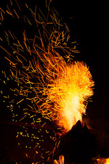 Flying sparks from fire against the night sky. Closeup of beautiful flame. Concept of travel and summer outdoor recreation. Soft focus.