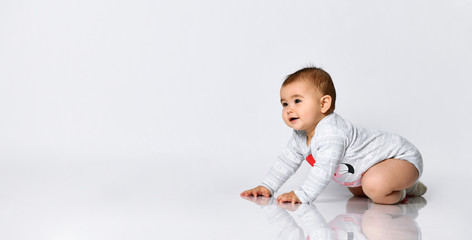 Little child in gray bodysuit and socks with red bow. She smiling, creeping on the floor isolated on white. Copy space, close up