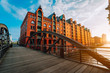 canvas print picture - Arch bridge over canals in the Speicherstadt of Hamburg. Warm evening sun light on red brick building