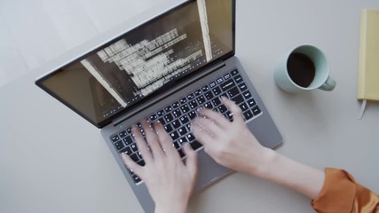 Timelapse top shot of hands of anonymous female programmer sitting and working at desk in office, typing computer code on laptop keyboard, and lines of digital symbols running on screen