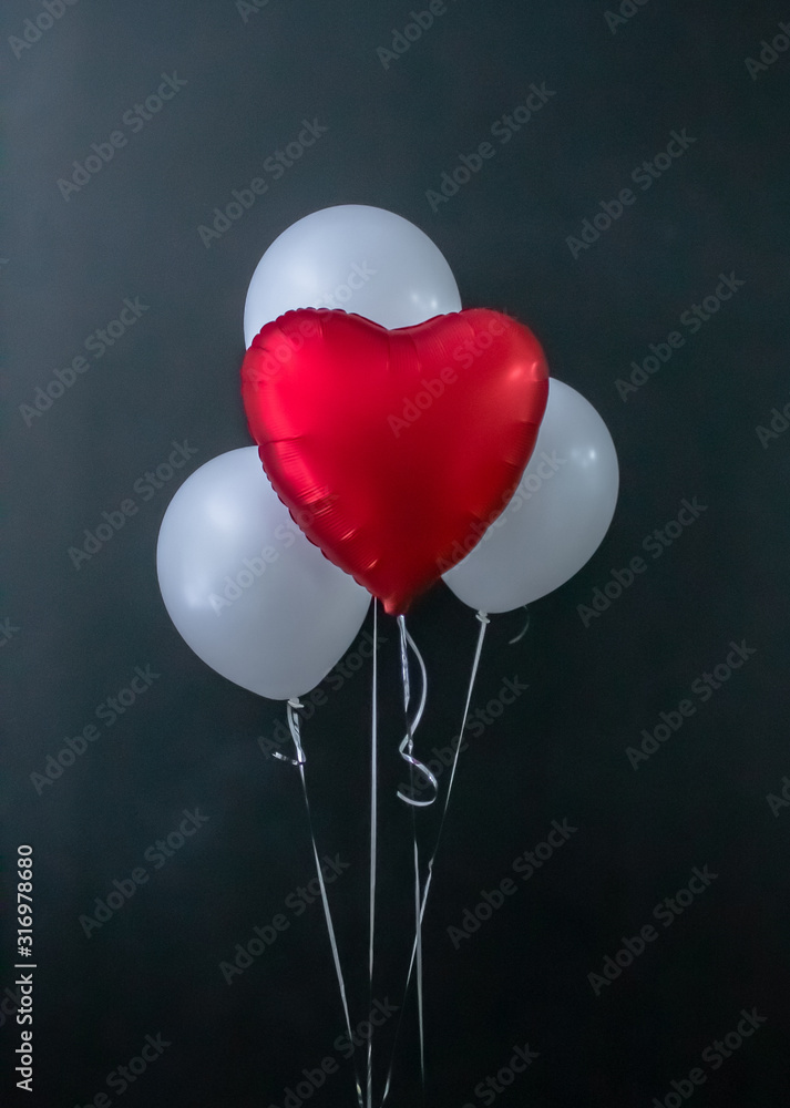 Red heart-shaped balloon and white round air balloons on a black ...
