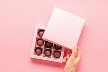 Female hand opens a box with sweets pink background . Gifts festive food love concept. Horizontal frame