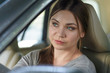 © Elena - Young attractive caucasian woman behind the wheel driving a car with displeased face expression. Bright blue eyes, dard hair, round shape face. Traffic jam concept or car accident. Copy space.