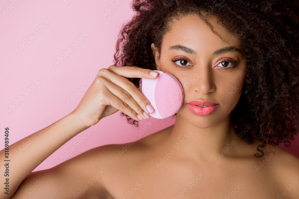 naked attractive african american girl with closed eyes using silicone cleansing facial brush, isolated on pink - obrazy, fototapety, plakaty 