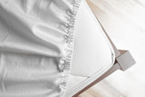 Fototapeta  - Bed corner with white fitted sheet. White sheet with elastic band. Flat sheet or bed cover.