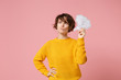 Pensive young brunette woman girl in yellow sweater posing isolated on pastel pink background studio portrait. People lifestyle concept. Mock up copy space. Hold say cloud with lightbulb, looking up.