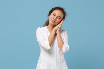 Wall Mural - African american doctor woman isolated on blue background. Female doctor in white medical gown sleep with folded hands under cheek. Healthcare personnel health medicine concept. Mock up copy space.