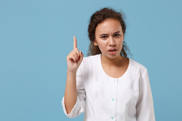 Wall Mural - Concerned african american doctor woman isolated on blue wall background. Female doctor in white medical gown holding index finger up. Healthcare personnel health medicine concept. Mock up copy space.