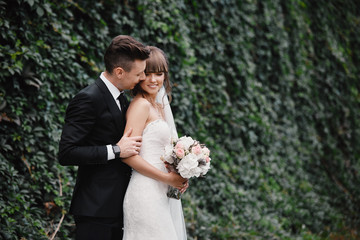 Wall Mural - Bride and groom at wedding Day walking Outdoors on spring green nature. Bridal couple, Happy Newlywed woman and man embracing in green park. Loving wedding couple outdoor. Bride and groom