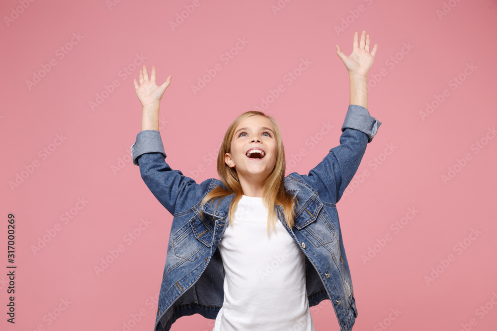 Cheerful little blonde kid girl 12-13 years old in denim jacket isolated on pastel pink background children studio portrait. Childhood lifestyle concept. Mock up copy space. Spreading rising hands up. - obrazy, fototapety, plakaty 