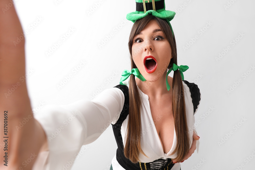 Funny young woman taking selfie on light background. St. Patrick's Day celebration