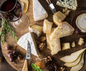 Wall Mural - Cheese platter with organic cheeses, fruits, nuts and wine on wooden table. Top view. Tasty cheese starter.
