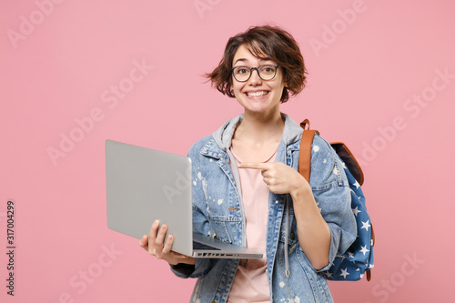 Fotomural Smiling young woman student in denim clothes eyeglasses backpack isolated on pastel pink background