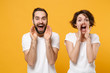 © ViDi Studio - Cheerful young couple friends bearded guy girl in white blank t-shirts posing isolated on yellow orange background. People lifestyle concept. Mock up copy space. Scream with hands gesture near mouth.