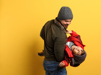 Canvas Print - Happy father and son in warm clothes playing on yellow background, space for text. Winter vacation