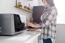 Cropped View Of Woman In Shirt Using Microwave In Kitchen