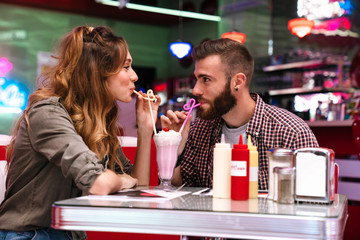 Poster - Loving couple sit in retro bright cafe drinking cockail indoors.