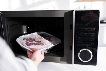 Wall Mural - cropped view of woman putting meat into microwave in kitchen