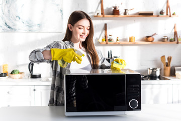 Wall Mural - smiling woman in rubber gloves cleaning microwave with sponge