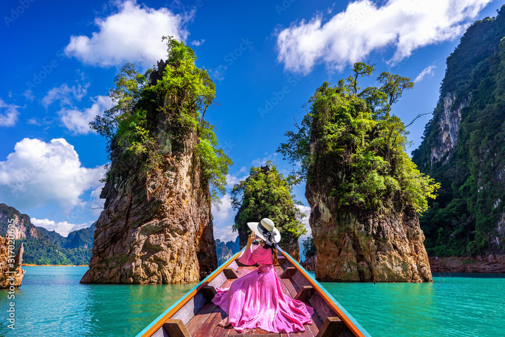 Beautiful girl sitting on the boat and looking to mountains in Ratchaprapha Dam at Khao Sok National Park, Surat Thani Province, Thailand. - obrazy, fototapety, plakaty 