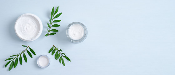 Wall Mural - jars of organic cosmetic cream and green leaves on blue background. organic natural cosmetic product