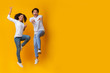 Funny Interracial Couple Jumping In Air On Yellow Background In Studio