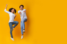 Funny Interracial Couple Jumping In Air On Yellow Background In Studio