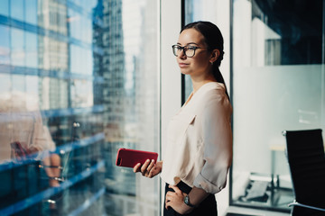 Businesswoman with smartphone in hand looking at window